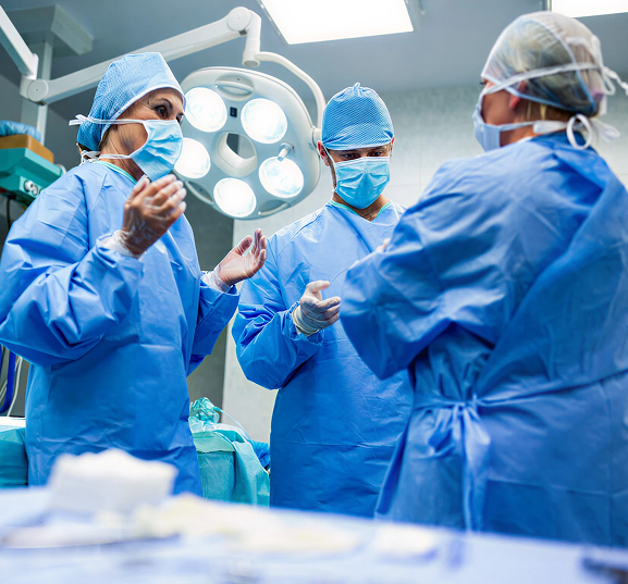 Three surgeons in blue scrubs and masks communicate under bright surgical lights in an operating room.