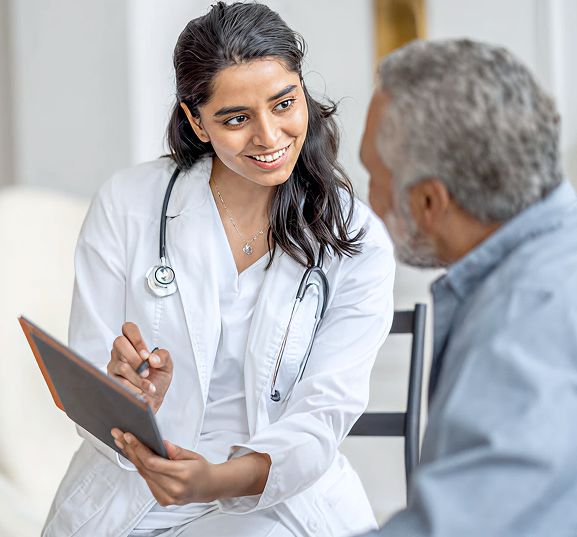 A smiling female doctor in a white coat shows a tablet to an older male patient, conveying a friendly and informative healthcare setting.