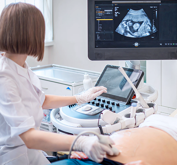 A healthcare professional performs an ultrasound on a pregnant individual's abdomen, displaying an image on a monitor. The setting is clinical and calm.