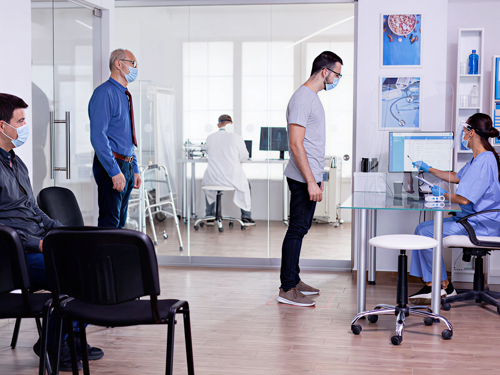 A medical clinic scene shows two masked patients waiting, one standing at a receptionist's desk. A nurse takes their information at a computer, while a doctor works in a background office. The atmosphere is calm and professional.