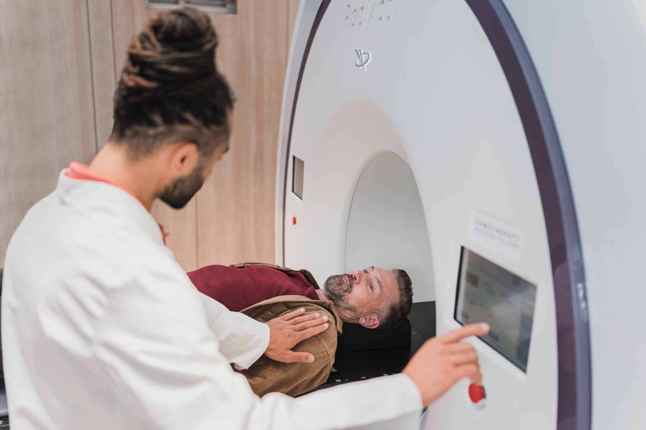 A patient lies inside an MRI scanner, looking calm. A doctor in a white coat operates the machine, focusing on the controls. The setting is clinical and professional.